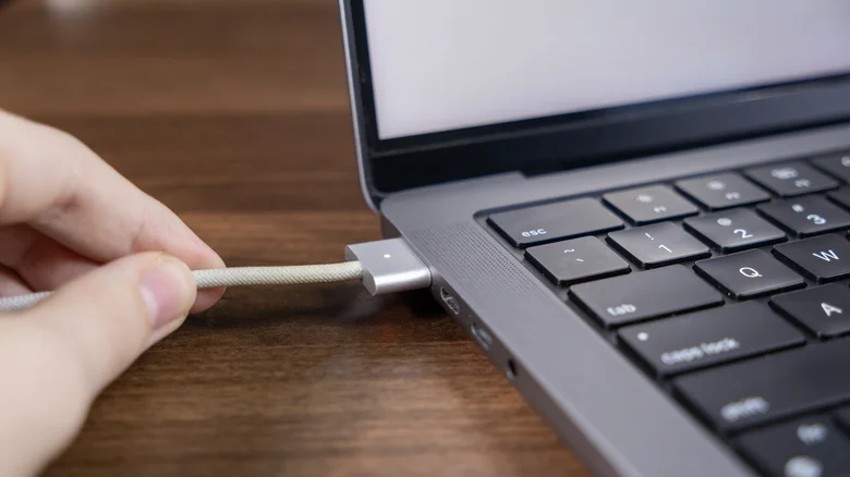 Hand pulling on a MagSafe cable attached to a MacBook.