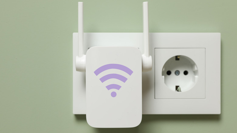 A Wi-Fi extender with  purple signal symbol is plugged into an outlet, against the backdrop of a green wall.