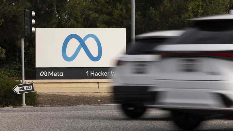 A sign with Meta's logo on it while cars drive by in front of it.