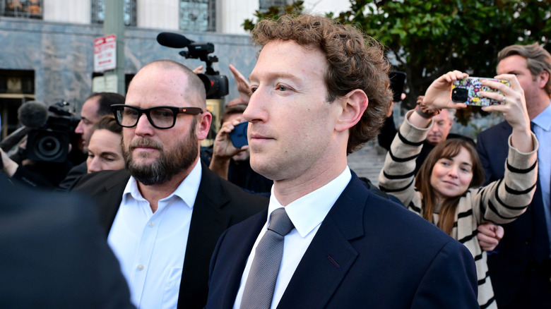Mark Zuckerberg in a suit surrounded by people.