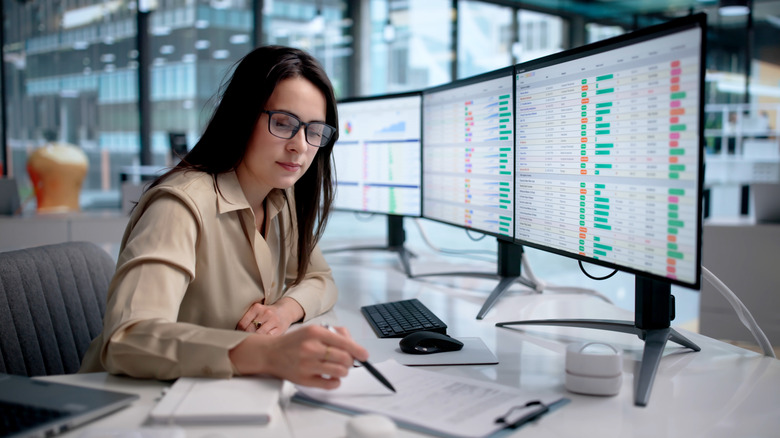A woman working in an office with spreadsheets on the monitors.