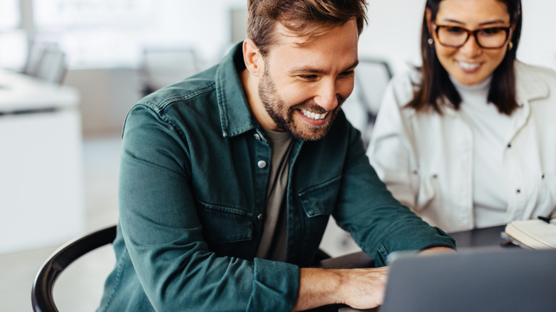 A millennial couple looking at laptop screen and smiling.