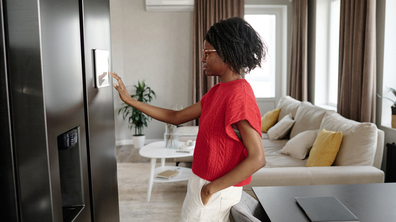 A woman in a kitchen touching a panel in a smart fridge.