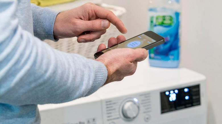 A man holding his phone in front of a washing machine.