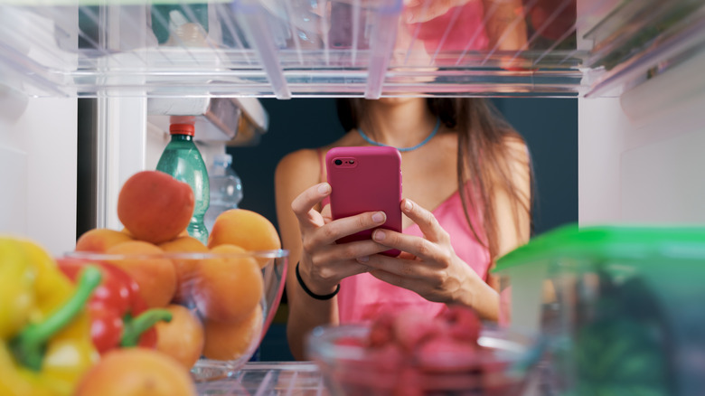 A woman putting her phone into the fridge