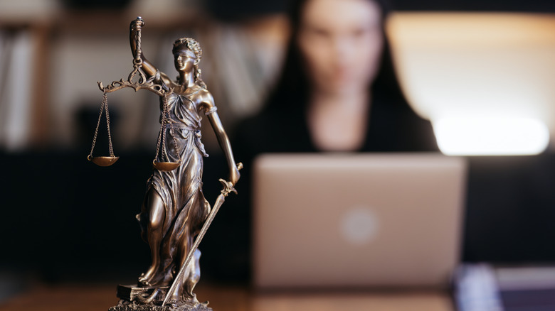 Statue of Justice with a blurred person working on a laptop in the background.