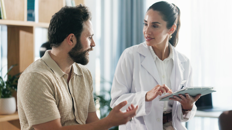 Doctor speaking to a man while holding a tablet.