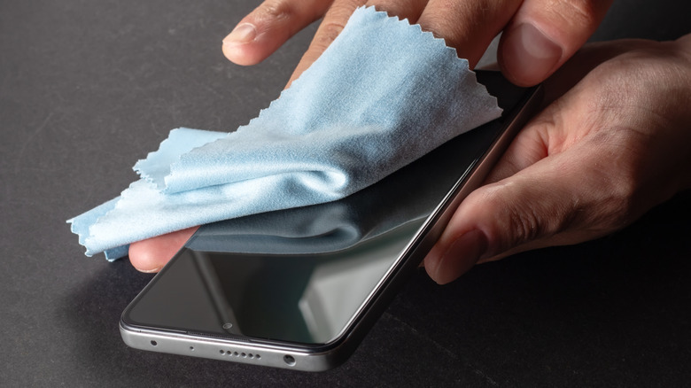 Person using microfiber cloth to wipe phone screen.