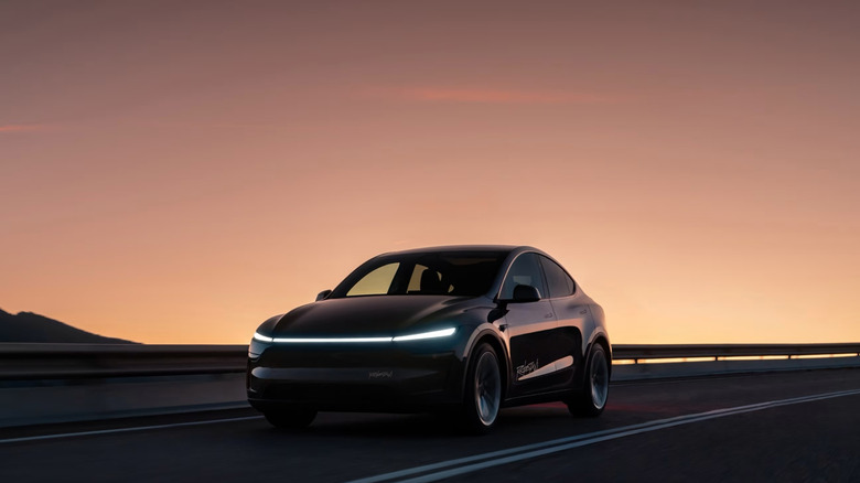A black Tesla robotaxi driving down a road at dusk.
