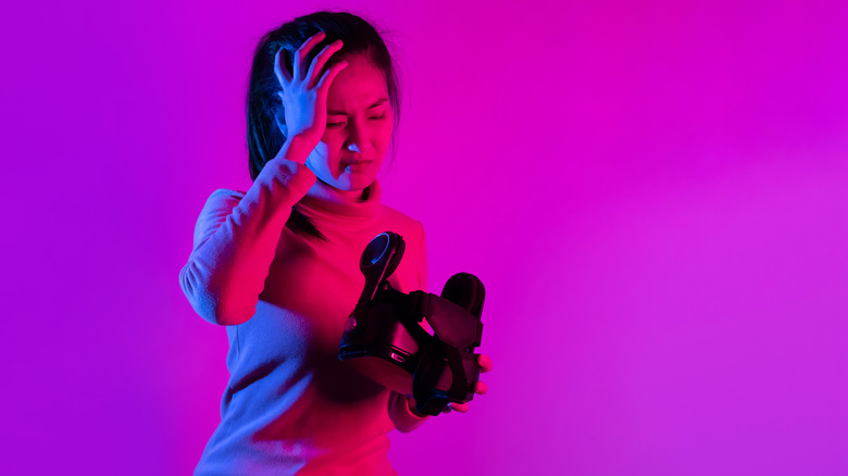 A woman feeling motion sick while holding a VR headset.