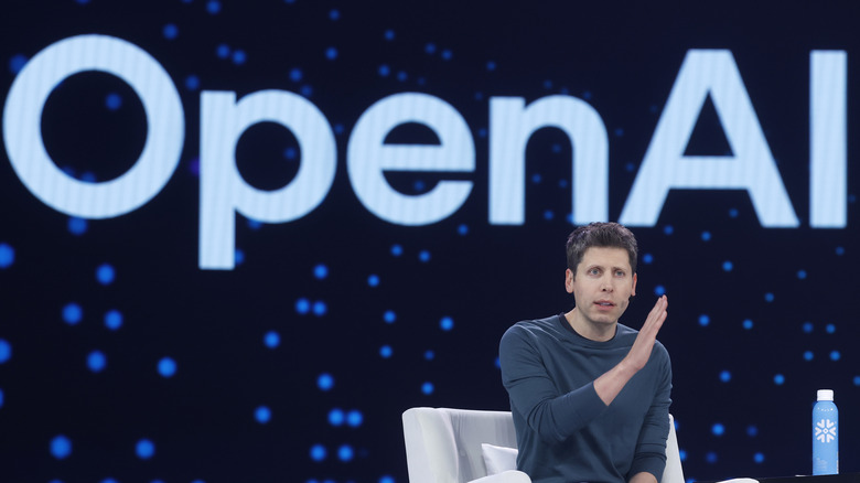 Photo of OpenAI CEO Sam Altman seated on stage in a white chair with the company's name on a blue screen behind him.