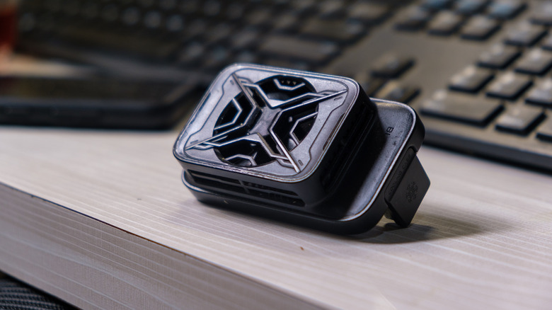 Peltier gaming phone cooler on a desk, near a smartphone and keyboard.
