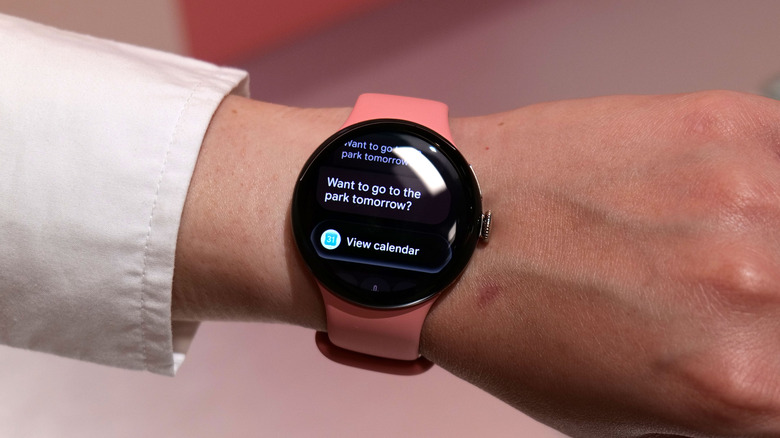 The Pixel Watch 5 with a peach strap on a person's wrist. Its screen shows a "View calendar" chip below a message asking about a visit to the park the next day.