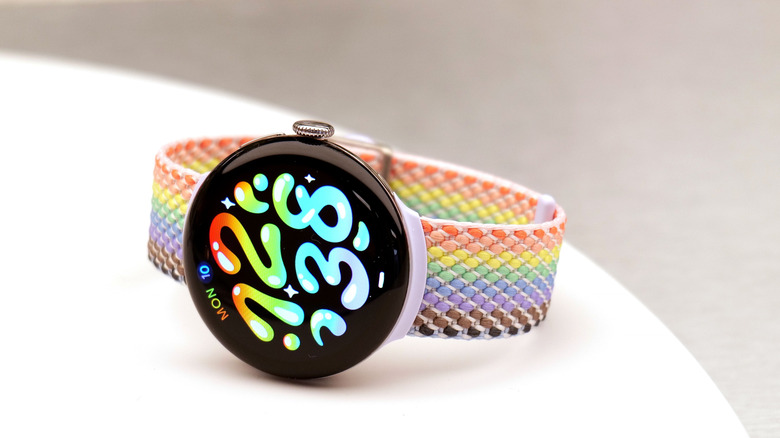 A Pixel Watch 5 with a rainbow band on a white table.