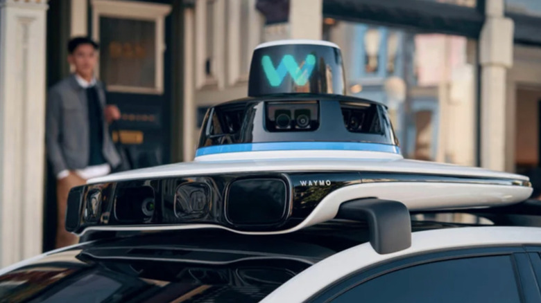 The top of a Waymo vehicle as a man looks on.