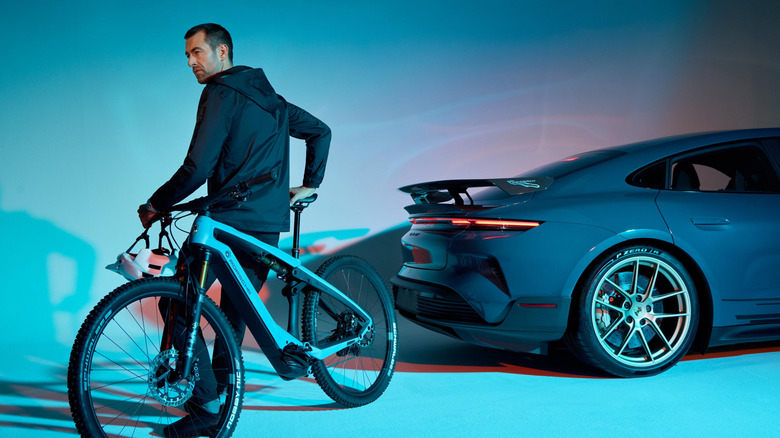 A man on a Porsche eBike next to a car.