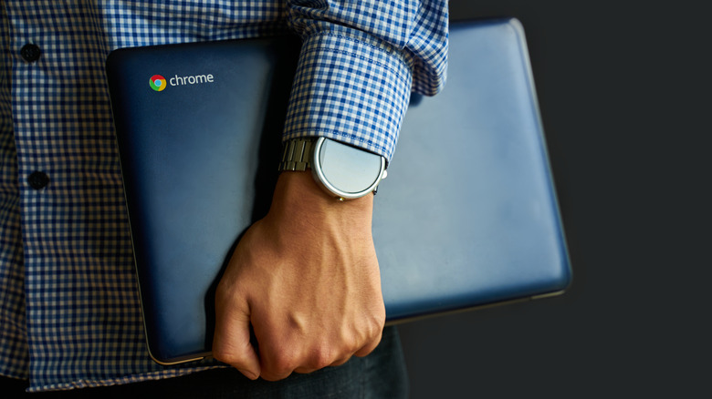 A man's hand holding a closed Chromebook.