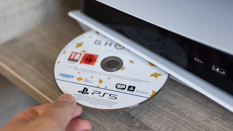 Close up of hand putting Ghost of Yotei physical disc into PS5 console