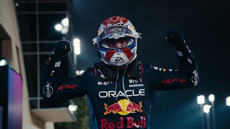 Still from Formula 1: Drive to Survive. A race car driver wearing full gear and helmet fist pumps both hands.