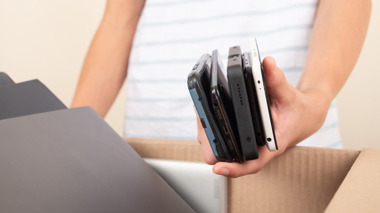Person holding several smartphones, about to put them into a cardboard box.