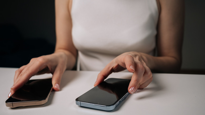 Woman with her hands holding two smartphones on a table.