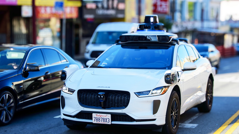 A white Waymo drives down a city street.