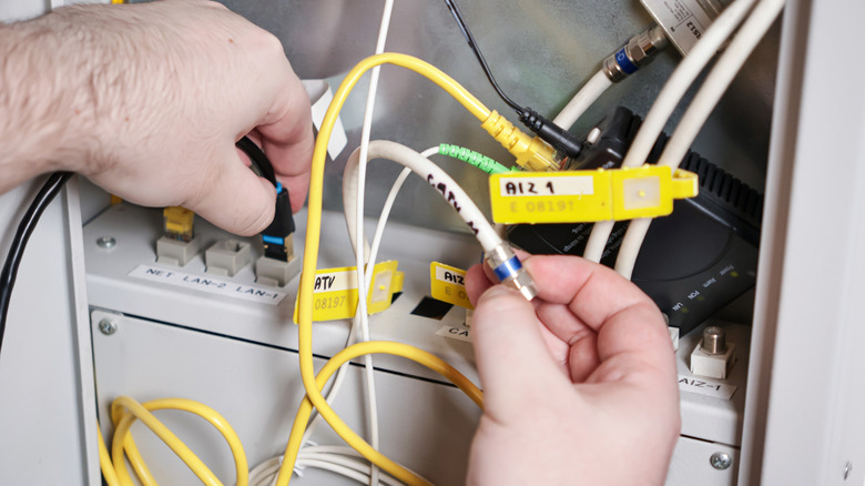 Hands moving various cables around inside an internet terminal.