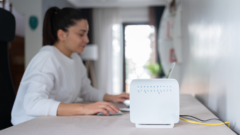 A Wi-Fi router sitting on a desk with a woman working in the background on a laptop.