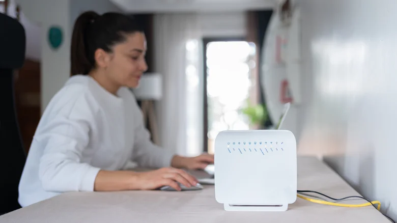 A Wi-Fi router sitting on a desk with a woman working in the background on a laptop.