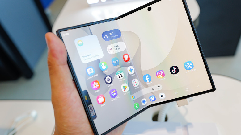 Hand holding a Samsung Galaxy Fold phone with One UI interface.