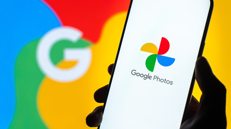 A smartphone displaying Google Photos logo with a large Google logo blurred in background.