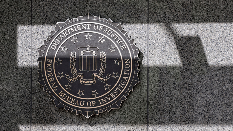 Photo of the J Edgar Hoover building's gray stone facade, with horizontal shadows cast over the insignia for the FBI.