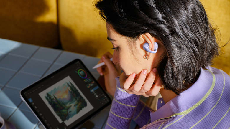 Closeup of a person, wearing the Shokz OpenDots Air earbuds, while sketching on a tablet