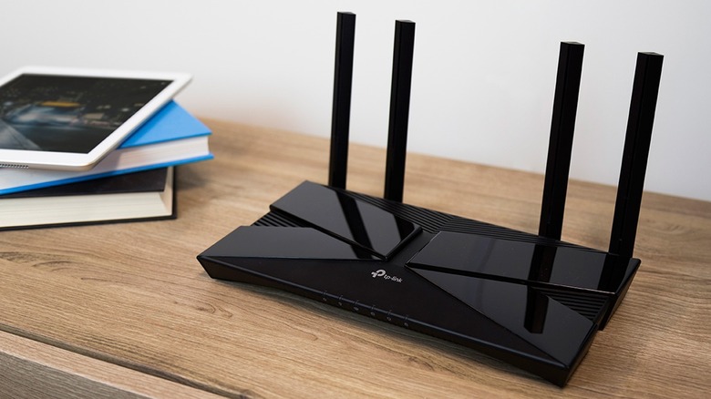 A TP-Link router sitting on a shelf next to a stack of books and an iPad mini