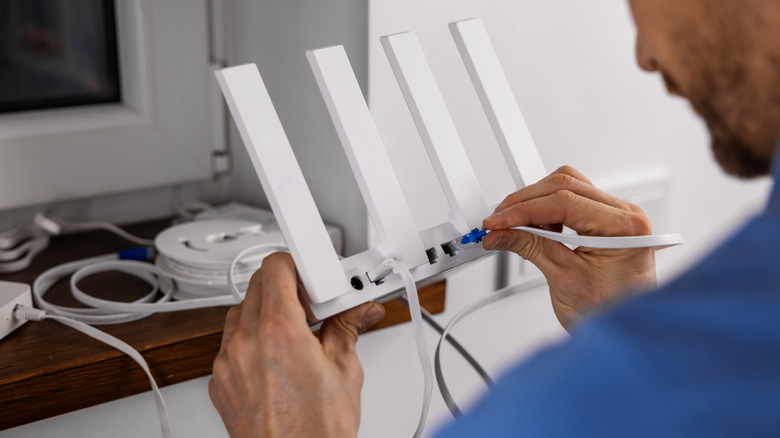 Man connecting an Ethernet cable to the back of a router.