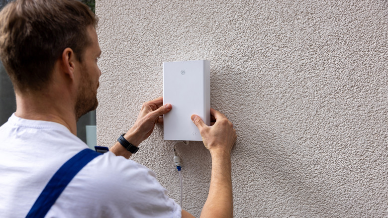 Technician installing a modem on the outside of a house.