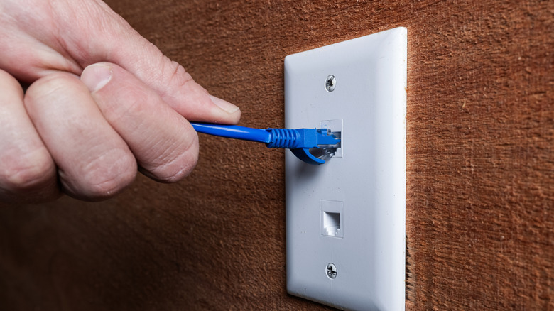 A person's hand connecting an Ethernet cable to a wall plug.