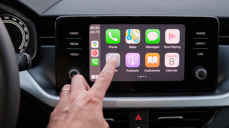 A finger pressing an active Apple CarPlay display.