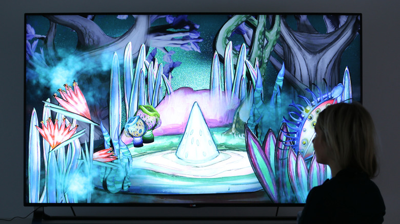 A woman stands before an OLED television showing a colorful, abstract piece of art.