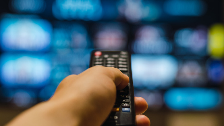 TV out of focus in background with a foregrounded hand holding its remote.