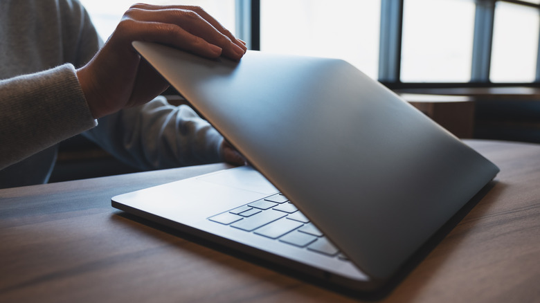 A hand closing a MacBook laptop at a desk.