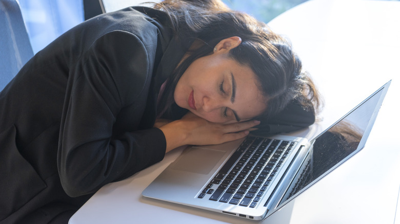 Woman sleeping at a table in front of a MacBook.