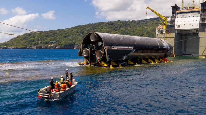 Crew in a boat face the Starship upper stage, cradled onto the submerged deck of the Forte transport ship