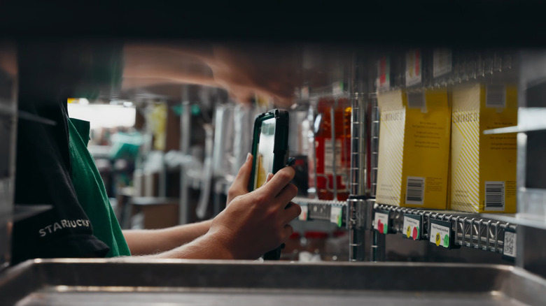 Profile view of a Starbucks workers scanning shelf items using a tablet