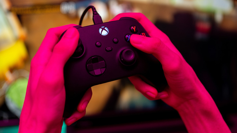 Hands holding a plugged-in black Xbox controller.