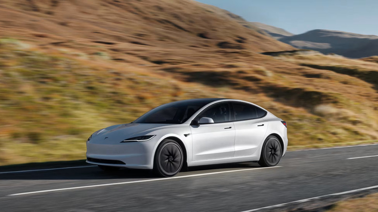 A white Model 3 driving on a highway.