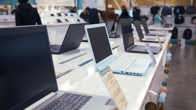 A line of laptops arrayed on a store shelf for display.