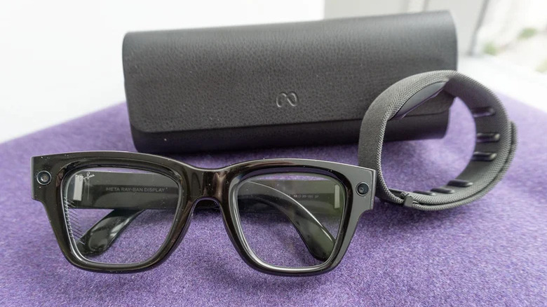 A pair of Meta Ray Ban Display glasses, its neural band and case, on a purple piece of cloth.