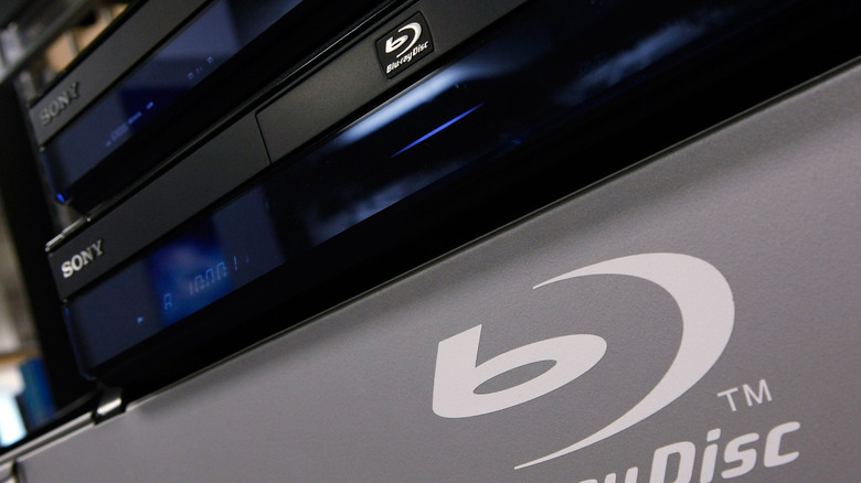 A collection of Sony Blu-ray players in a store with a large Blu-ray symbol in the foreground.