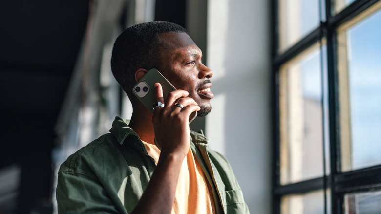 Man taking call on an iPhone in front of a window.